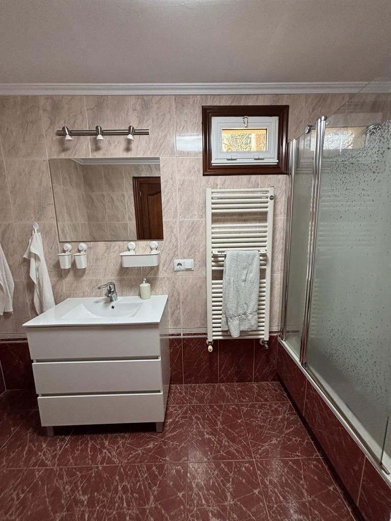 Baño con revestimiento de mármol rojo, lavabo blanco con mueble y mampara de vidrio
