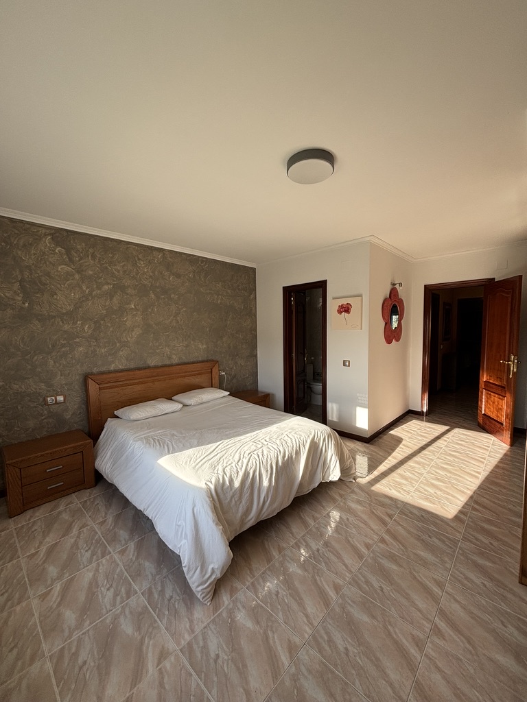 Dormitorio principal con pared de efecto piedra gris, cama de matrimonio y puerta a baño en suite