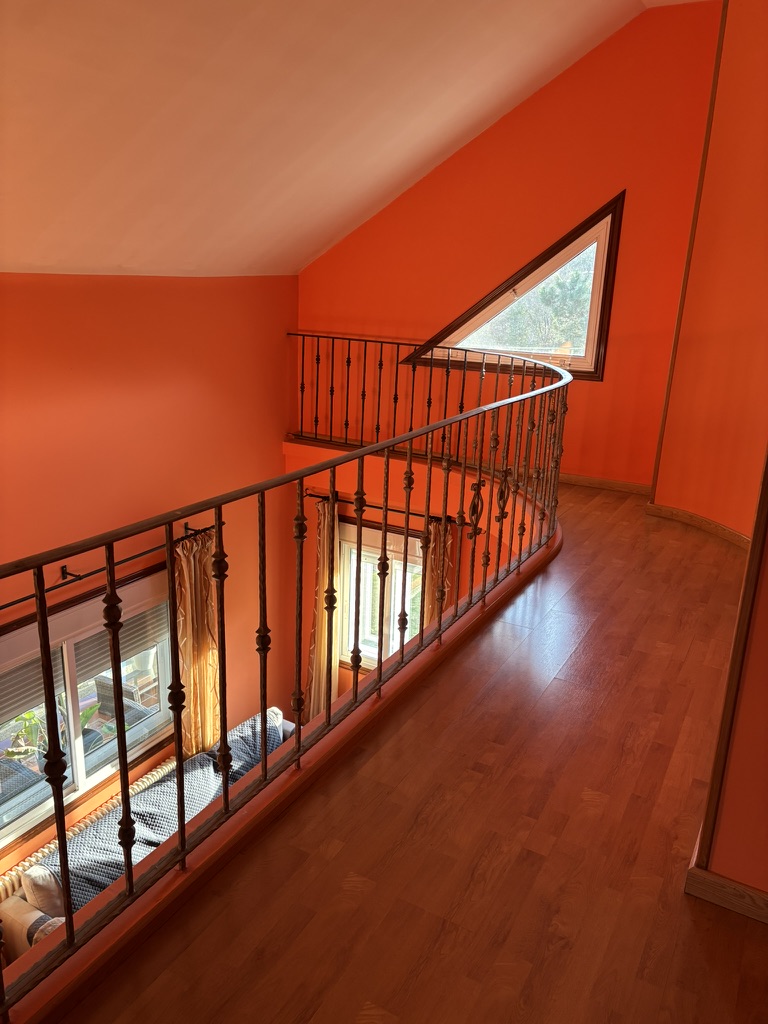 Galería superior con paredes en naranja terracota, barandilla de forja artesanal y ventana triangular característica