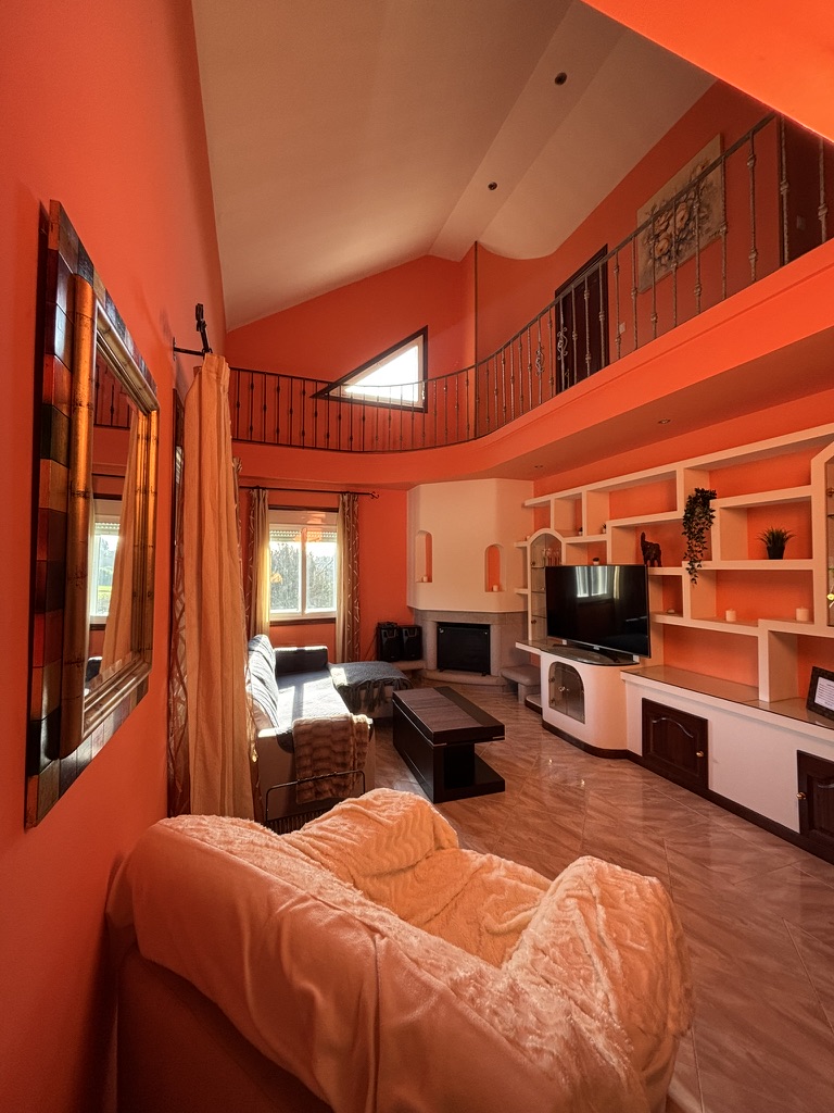Salón principal con techo abuhardillado, paredes en naranja terracota y galería superior con barandilla de forja